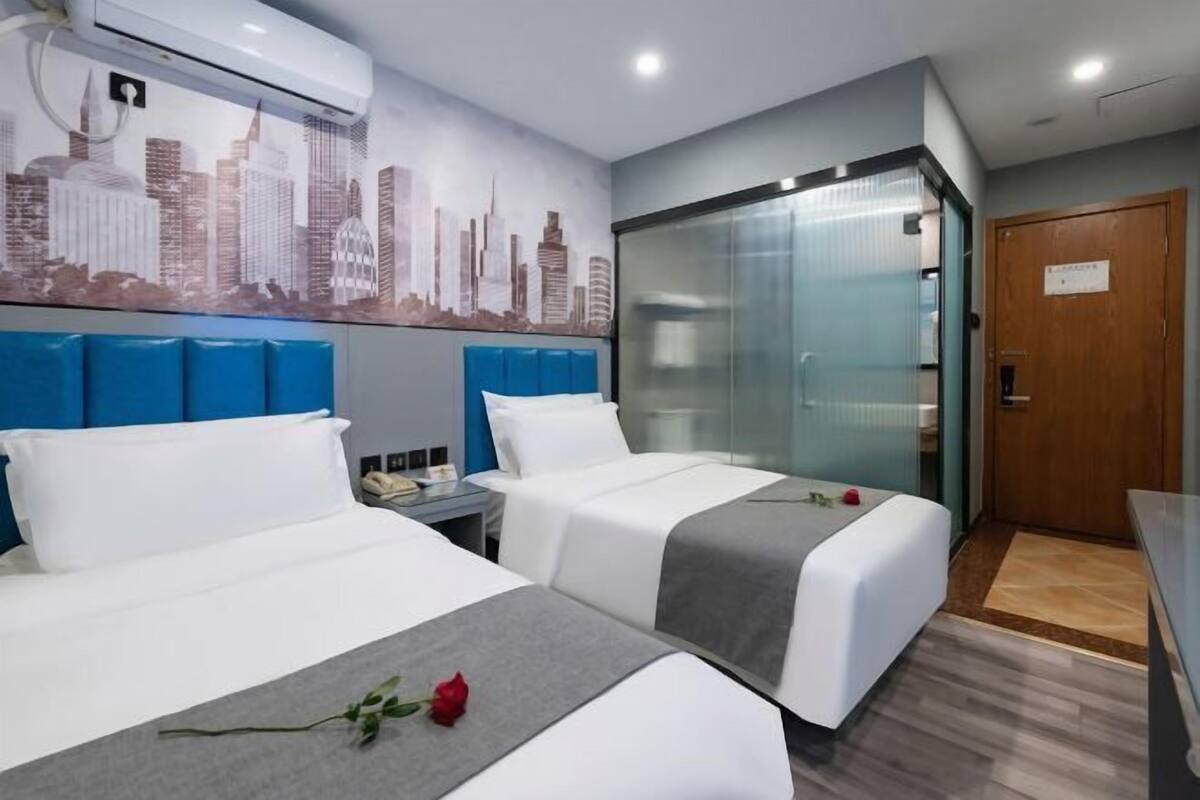 Quarto de hotel com duas camas, um mural com vista para a cidade, um painel de vidro e uma porta de madeira.