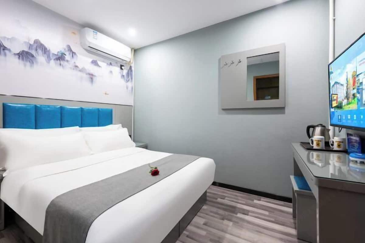 Quarto de hotel com cama, escrivaninha, televisão e ar condicionado fixado na parede.