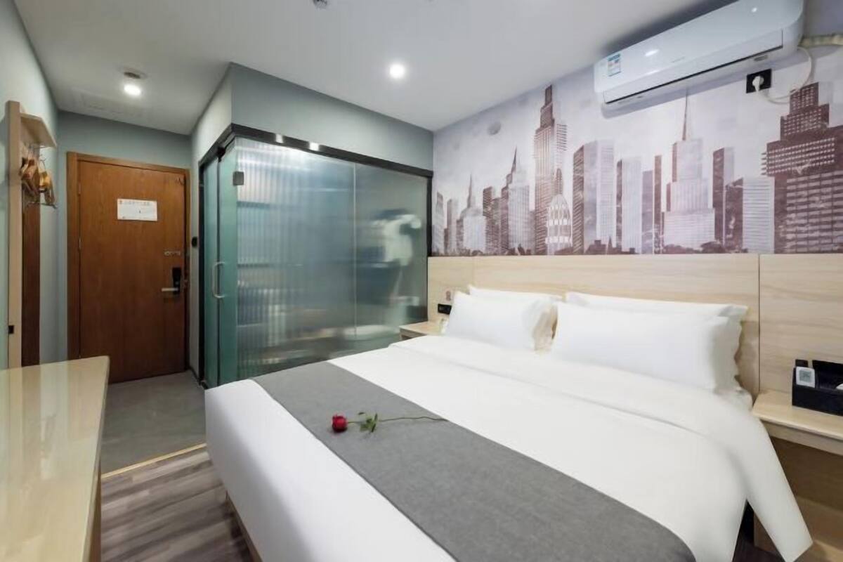 Quarto de hotel com cama, escrivaninha, elevador de vidro e um mural com vista para a cidade.