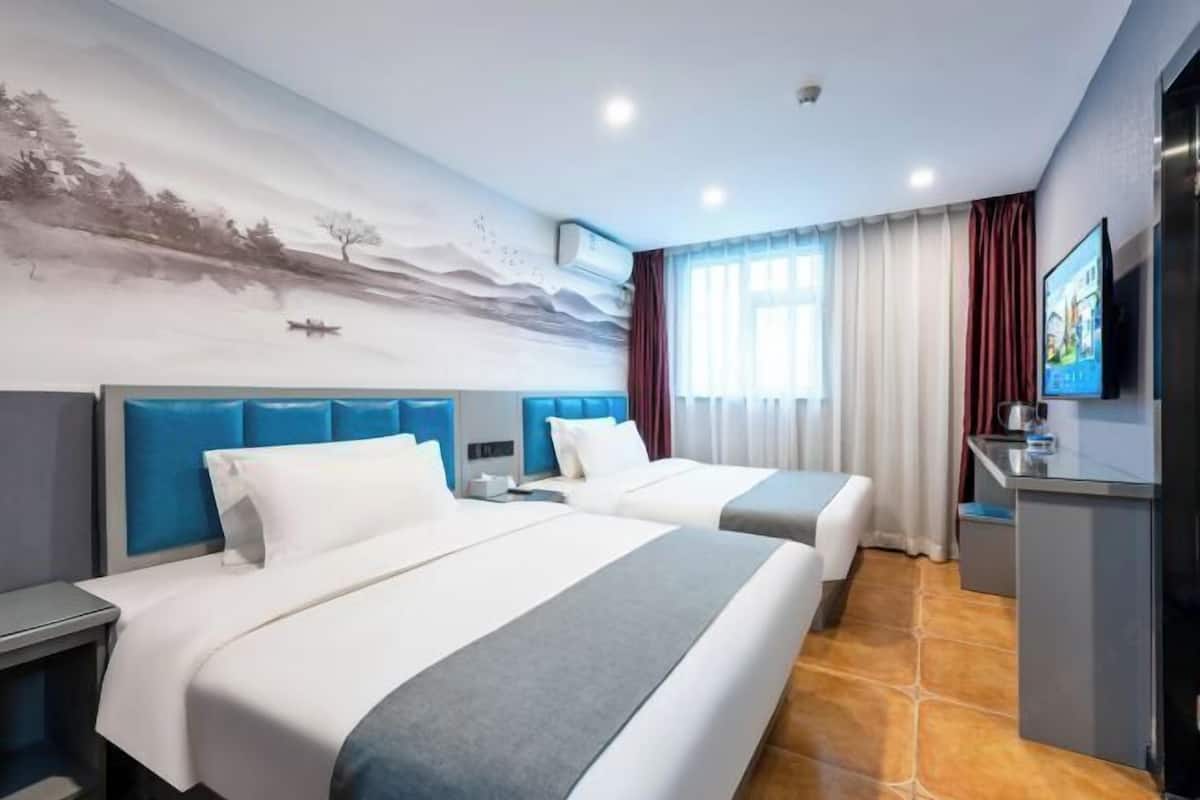 Quarto de hotel com duas camas, televisão, escrivaninha e um mural na parede.