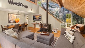 A modern living room with a fireplace, a dining area, and a staircase leading to an upper level. - Forest+Mountain Views, Hot Tub, Sauna, EV Charger, Dogs OK, Near Lake Wenatchee (Leavenworth)