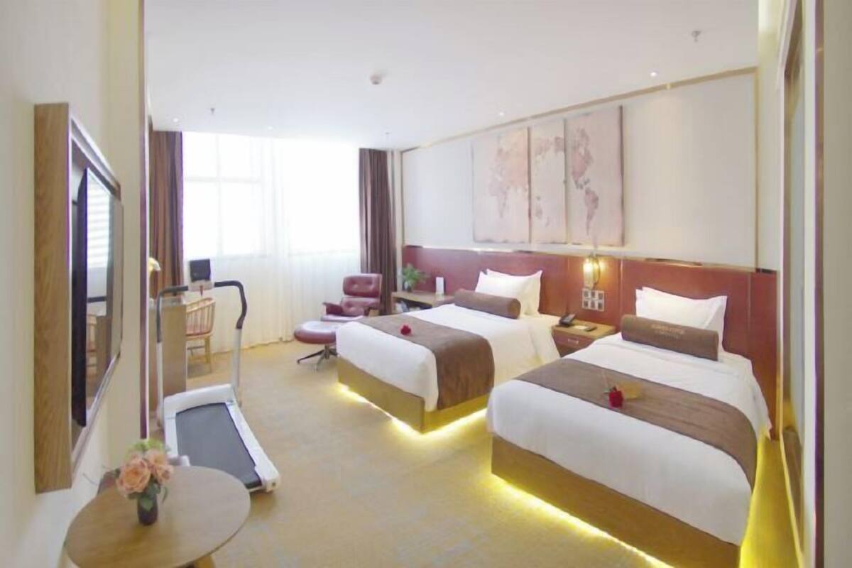 Habitación de hotel con dos camas, un escritorio, una silla, una cinta de correr y obras de arte en las paredes.