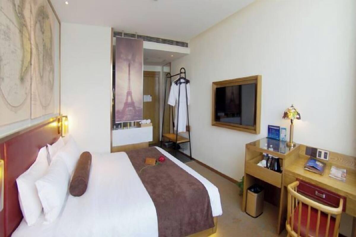 Una habitación de hotel con cama, escritorio, silla, televisor y espejo.