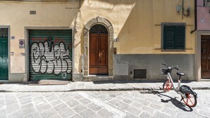 A street with a bicycle parked by a building with a wooden door and a green shutter. - Residenza Pinzochere (Firenze)