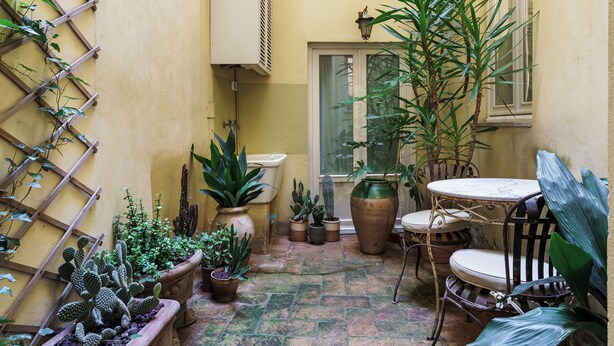 A courtyard with a variety of potted plants, a wooden ladder, a table with chairs, and a window. - Residenza Pinzochere (Firenze)