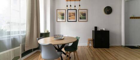 A dining area with a round wooden table, grey and green chairs, a black cabinet, and framed pictures on the wall.