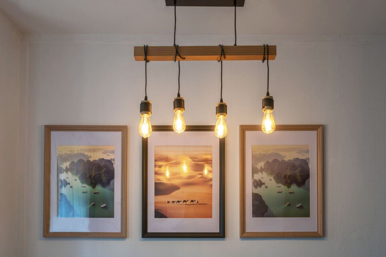 A wall with three framed pictures and a hanging light fixture with four bulbs.