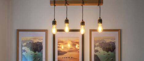 A wall with three framed pictures and a hanging light fixture with four bulbs.