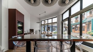 A modern kitchen with a glass dining table and clear chairs, large windows, and a view of the street. - Maison design hyper centre - Triangle d'or (Vichy)