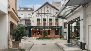 A narrow street with a building featuring a traditional European architectural style, a sign for a restaurant, and a modern glass building to the right. - Maison design hyper centre - Triangle d'or (Vichy)