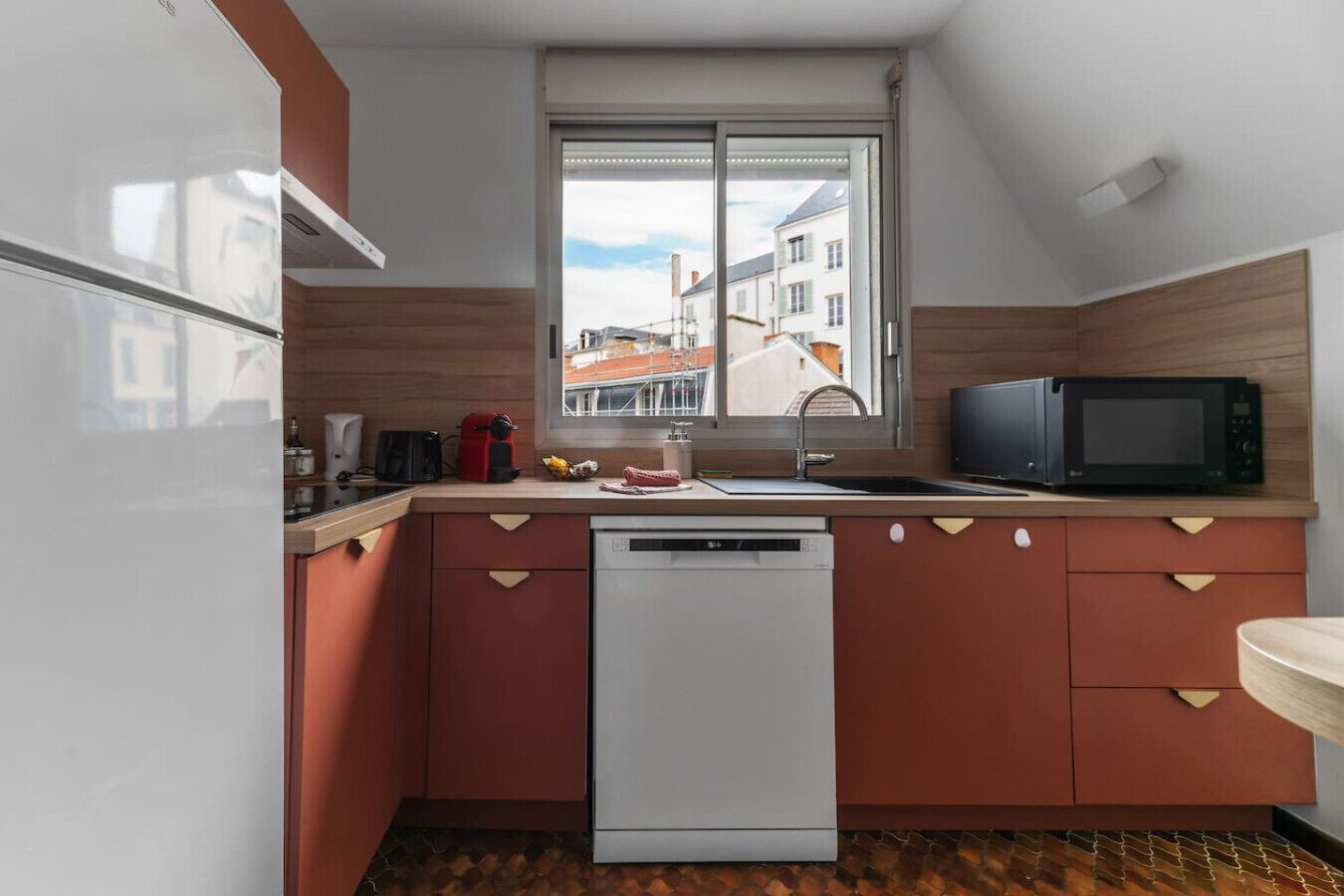 A compact kitchen with a dishwasher, a microwave, and a window with a view of buildings.