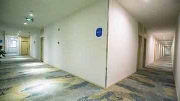 A long, narrow hotel corridor with a patterned carpet, doors on both sides, and a blue sign on the wall.