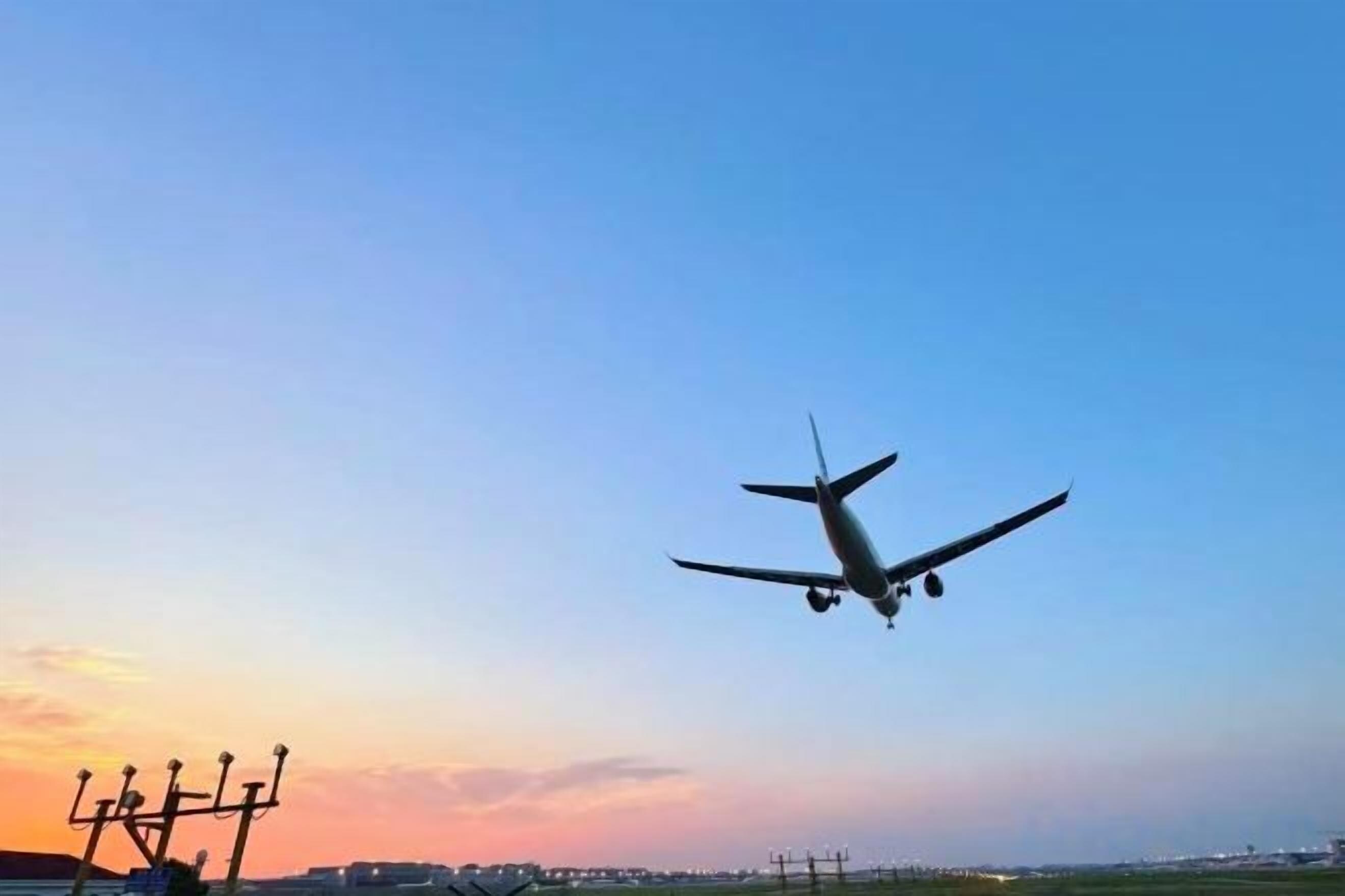 An airplane in flight with airport infrastructure in the background.