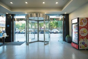 A hotel entrance with a revolving door, a vending machine, and a view of parked cars outside. - Weiting Qingju Hotel (Shanghai Hongqiao Airport Beihua Road Branch) (Shanghai)