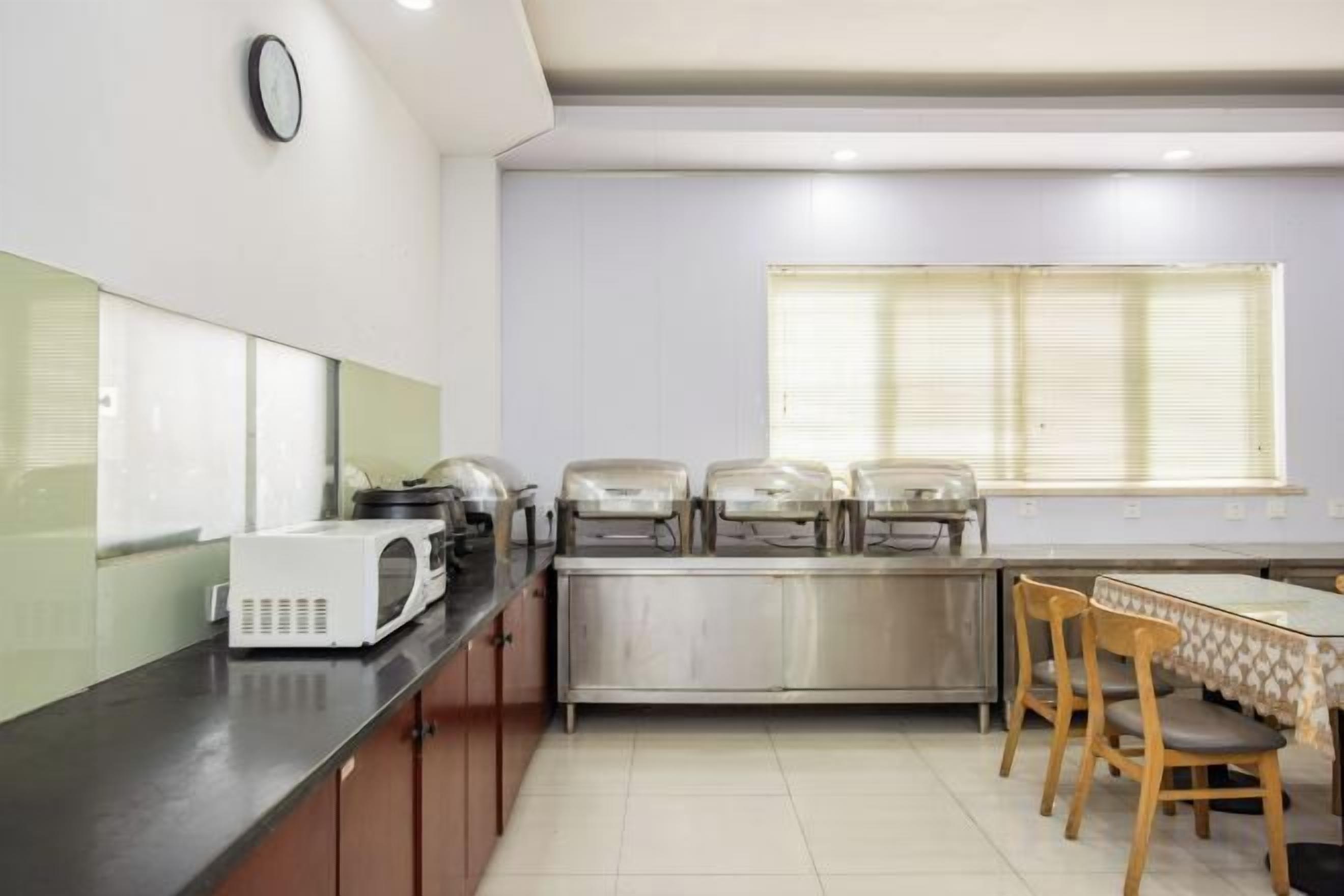 A kitchen with a microwave, toaster, and food warmer on the counter, a dining table with chairs, and a window with blinds.