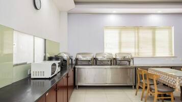 A kitchen with a microwave, toaster, and food warmer on the counter, a dining table with chairs, and a window with blinds.