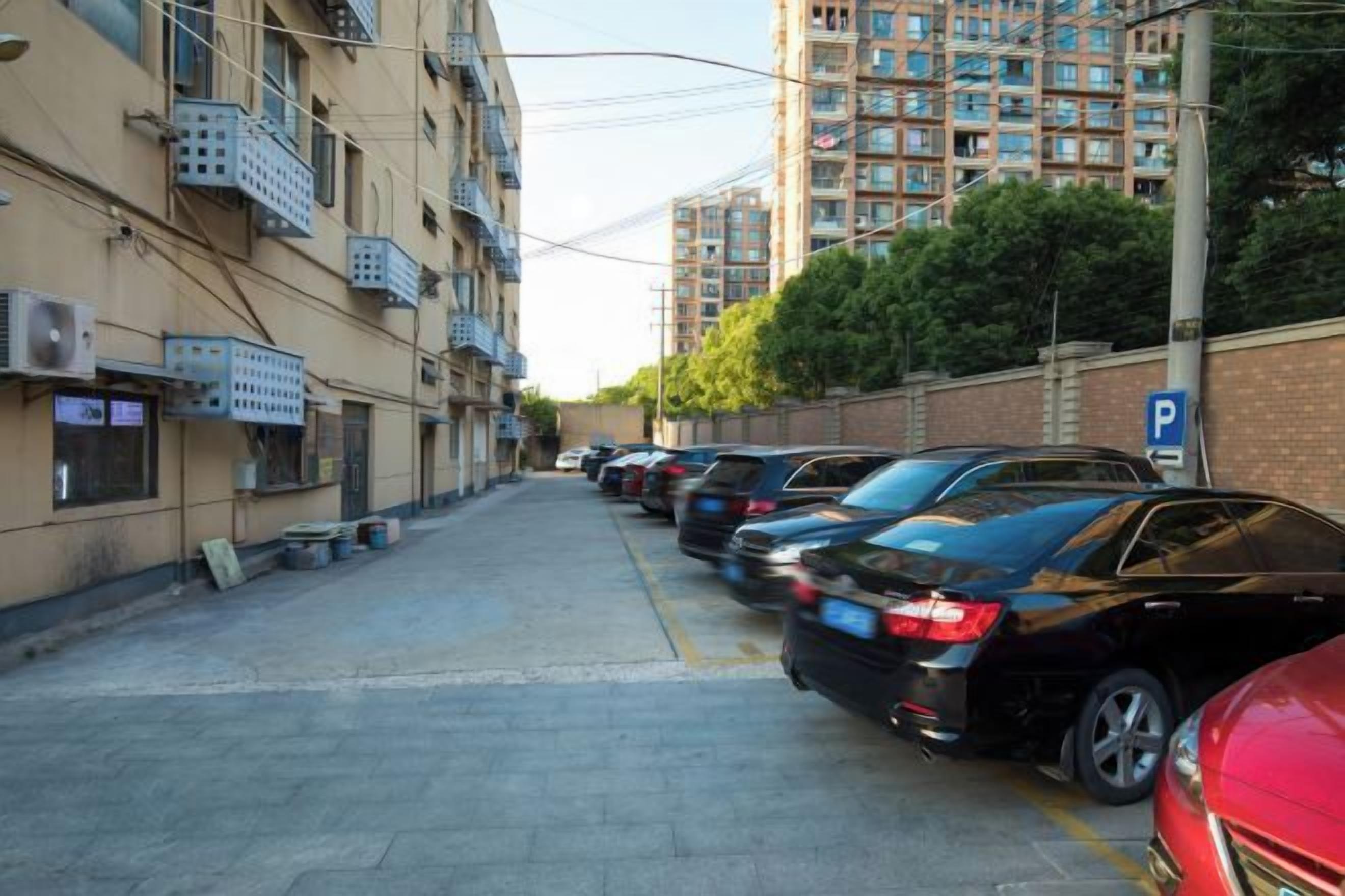 Una calle estrecha flanqueada por coches aparcados y edificios de varios pisos con balcones.