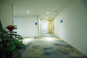 Un couloir d’hôtel avec un tapis à motifs, une plante en pot et des panneaux indicateurs sur les murs.