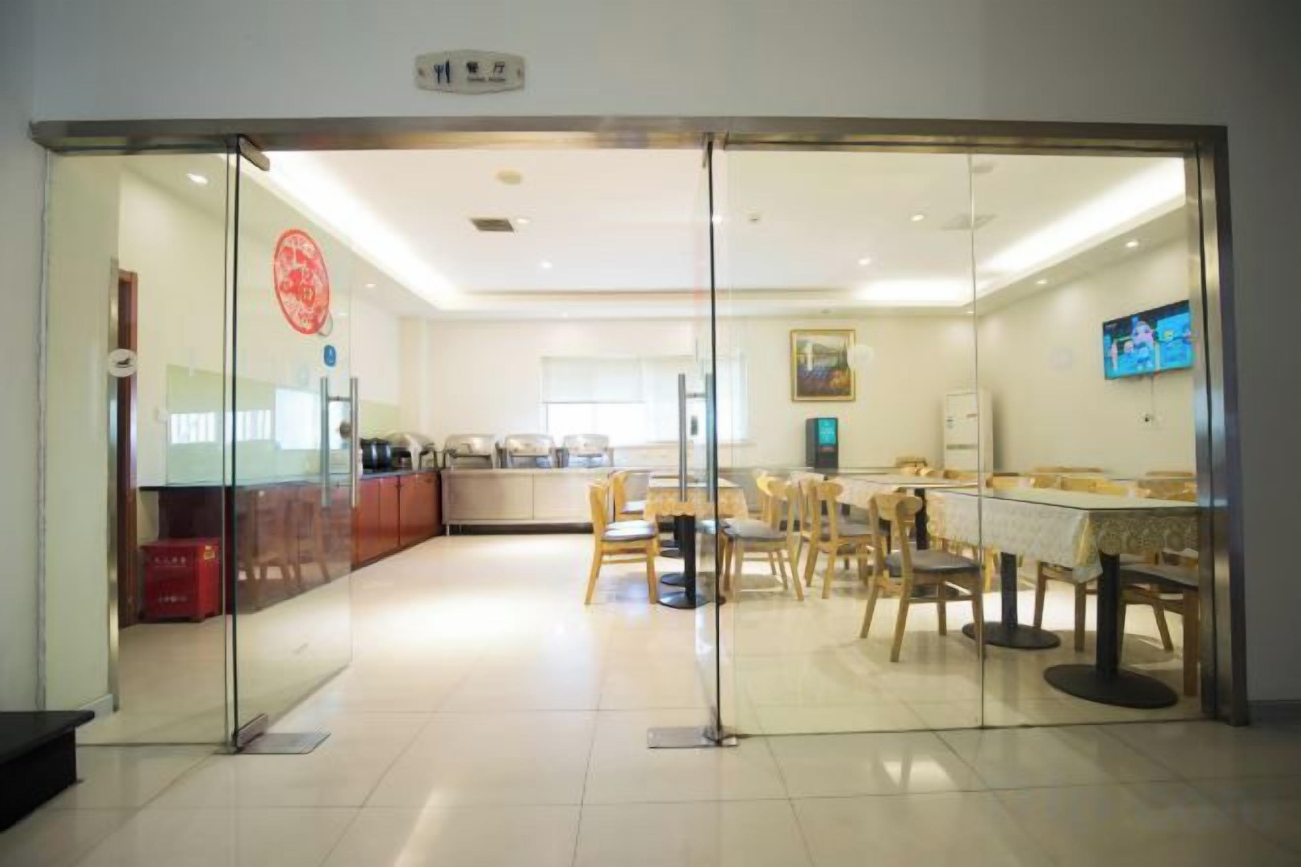 Ein modernes Interieur mit einer Glastrennwand, einem Essbereich mit Tischen und Stühlen sowie einer Küche im Hintergrund.