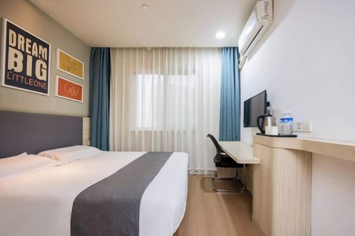 A hotel room with a bed, a desk, a chair, a television, and an air conditioning unit.