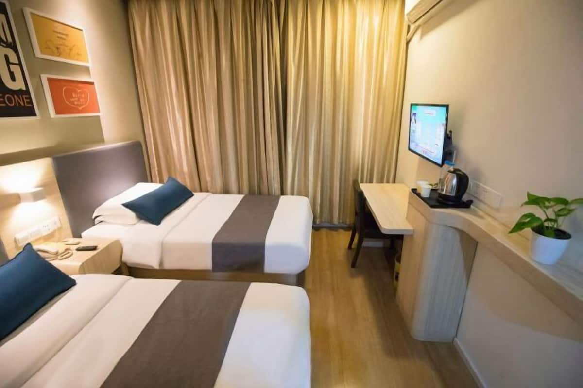 A hotel room with two beds, a desk, a chair, a TV, and a plant.