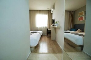 Una camera d'albergo con due letti, una scrivania con una sedia, una finestra con tende e un televisore a parete.