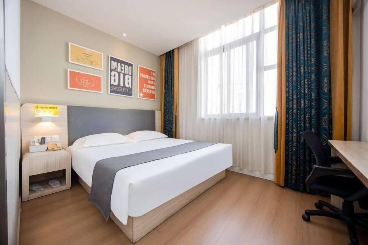 A hotel room with a bed, bedside table, lamp, and a desk with a chair.