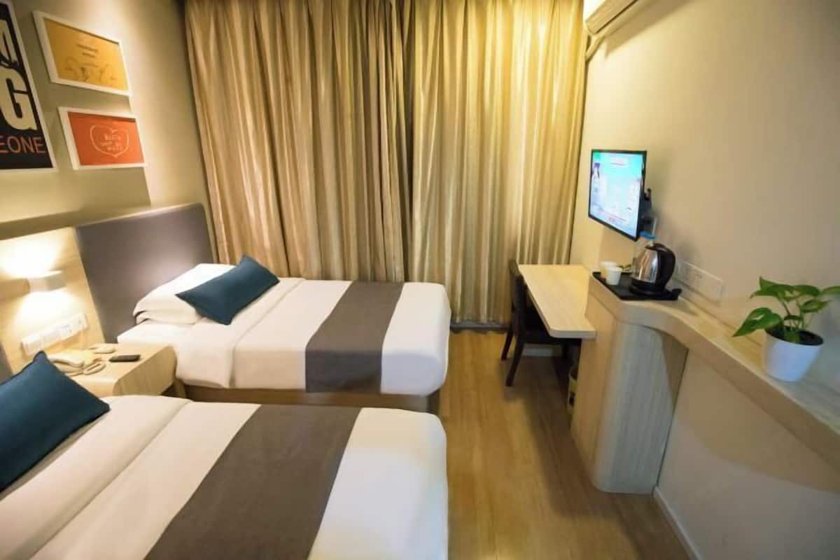 A hotel room with two beds, a desk, a TV, and a plant.