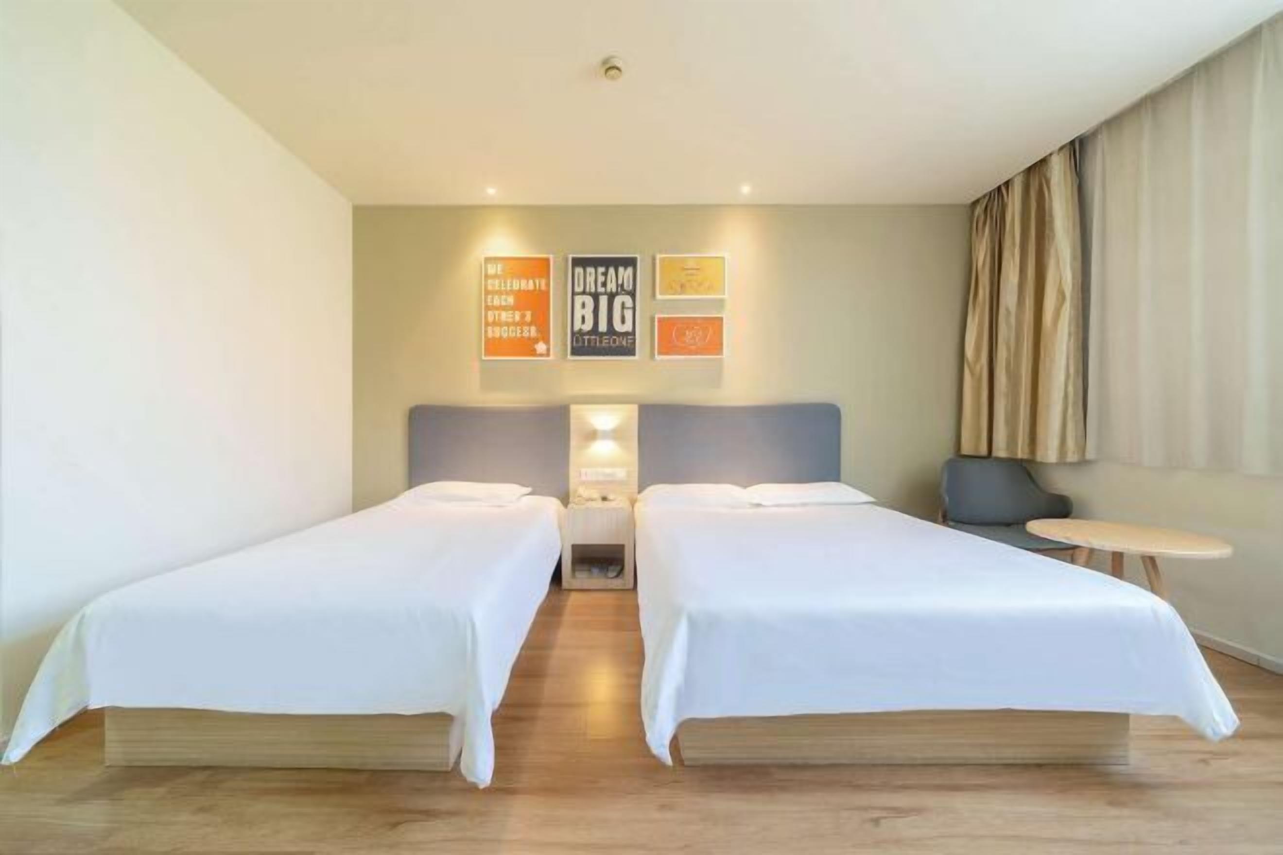 A hotel room with two beds, a nightstand, a small table, and a wall with motivational posters.
