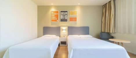 A hotel room with two beds, a nightstand, a small table, and a wall with motivational posters.