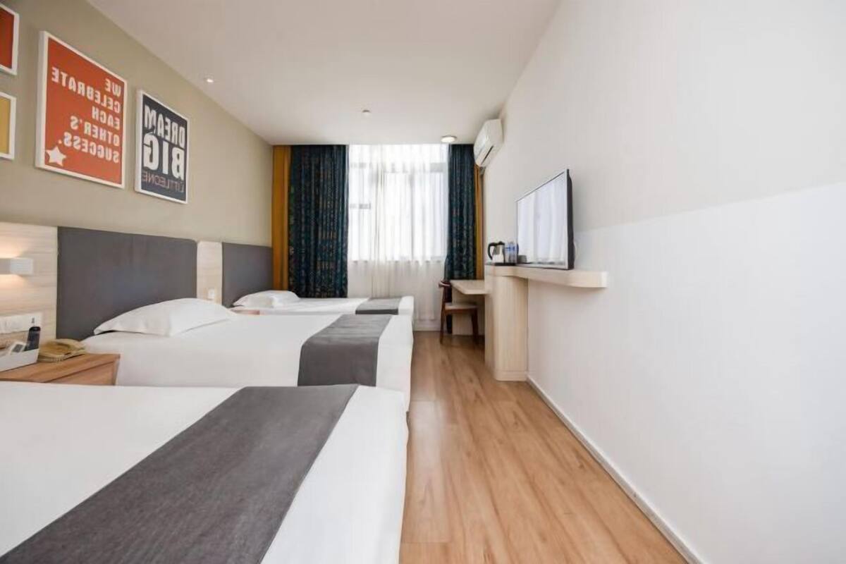 A hotel room with two beds, a desk, a chair, a TV, and a window with curtains.