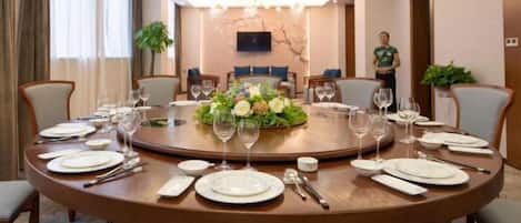 Un salón de conferencias con una mesa redonda dispuesta para una reunión, equipado con sillas, un televisor y un centro de mesa floral.