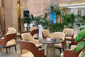 Un hall d'hôtel avec des tables et des chaises rondes, des plantes d'intérieur et un aménagement intérieur moderne.