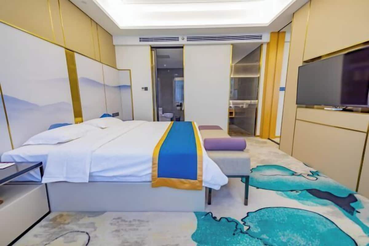 Ein Hotelzimmer mit Bett, Schreibtisch, Fernseher und einem durchgehenden Tür sichtbaren Badezimmer.