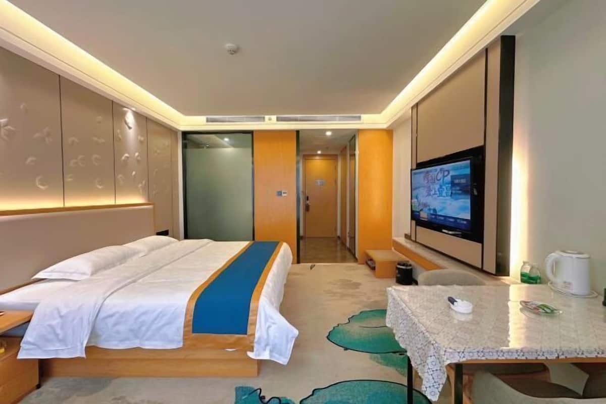 Ein Hotelzimmer mit einem Bett, einem Fernseher, einem Tisch mit Wasserkocher und einer Tür zu einem anderen Zimmer.