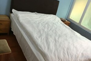 A bed with a white bedspread, a wooden nightstand, and a window with blinds. - Jincheng Hostel (Shanghai)