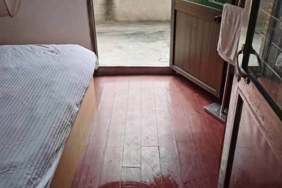 A room with a bed, a wooden cabinet, and a view of the outside.