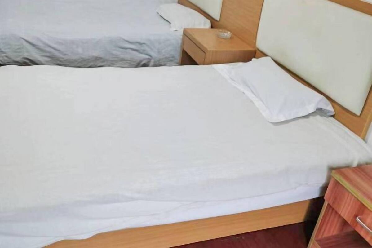 A double bed with white linens, a wooden headboard, and a bedside table with a lamp.