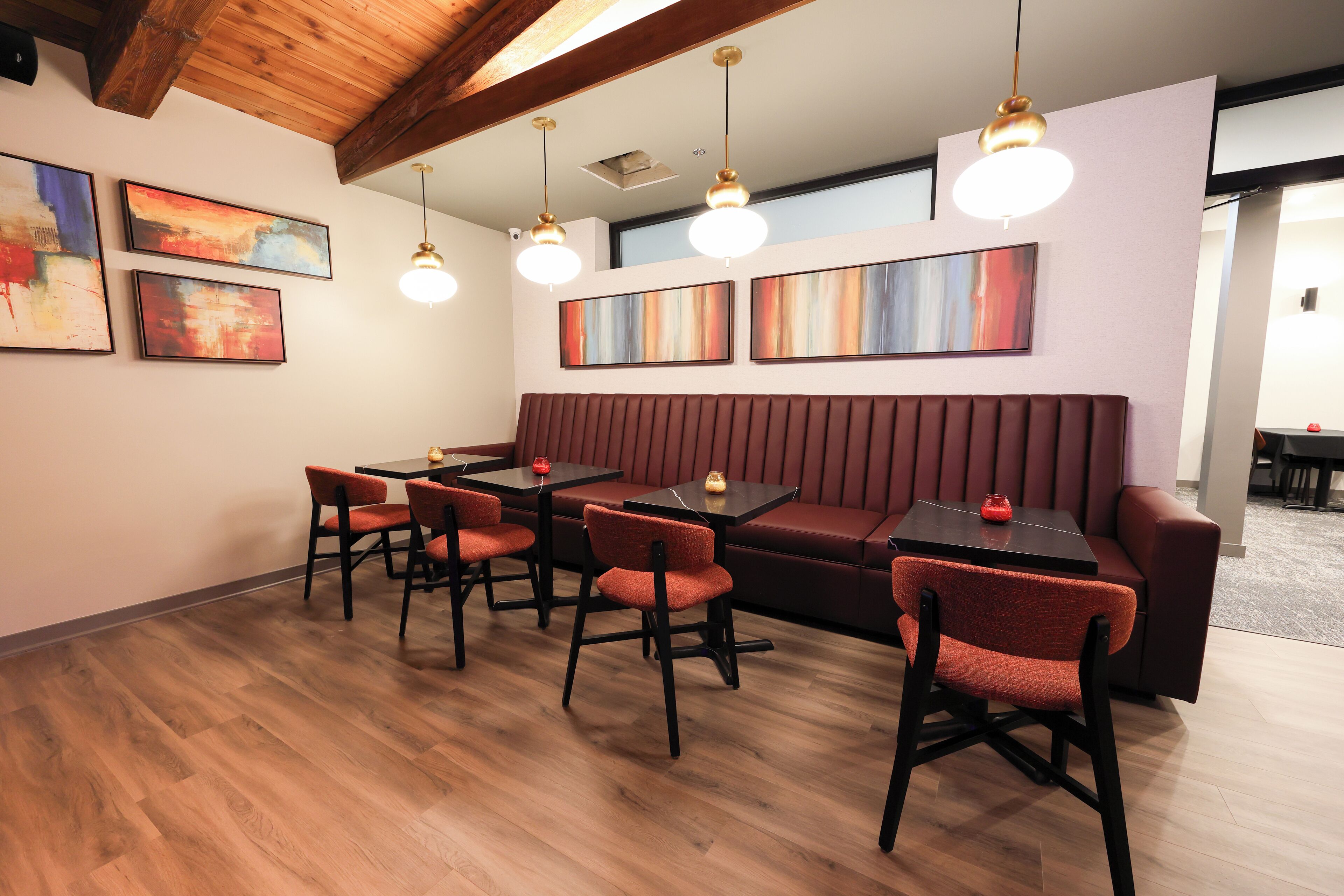 A modern dining area with wooden flooring, red upholstered seating, and pendant lighting.