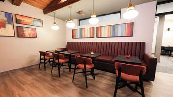 A modern dining area with wooden flooring, red upholstered seating, and pendant lighting.