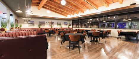 Un restaurante espacioso con techos de madera, varias mesas y sillas para comer, y una zona de bar.