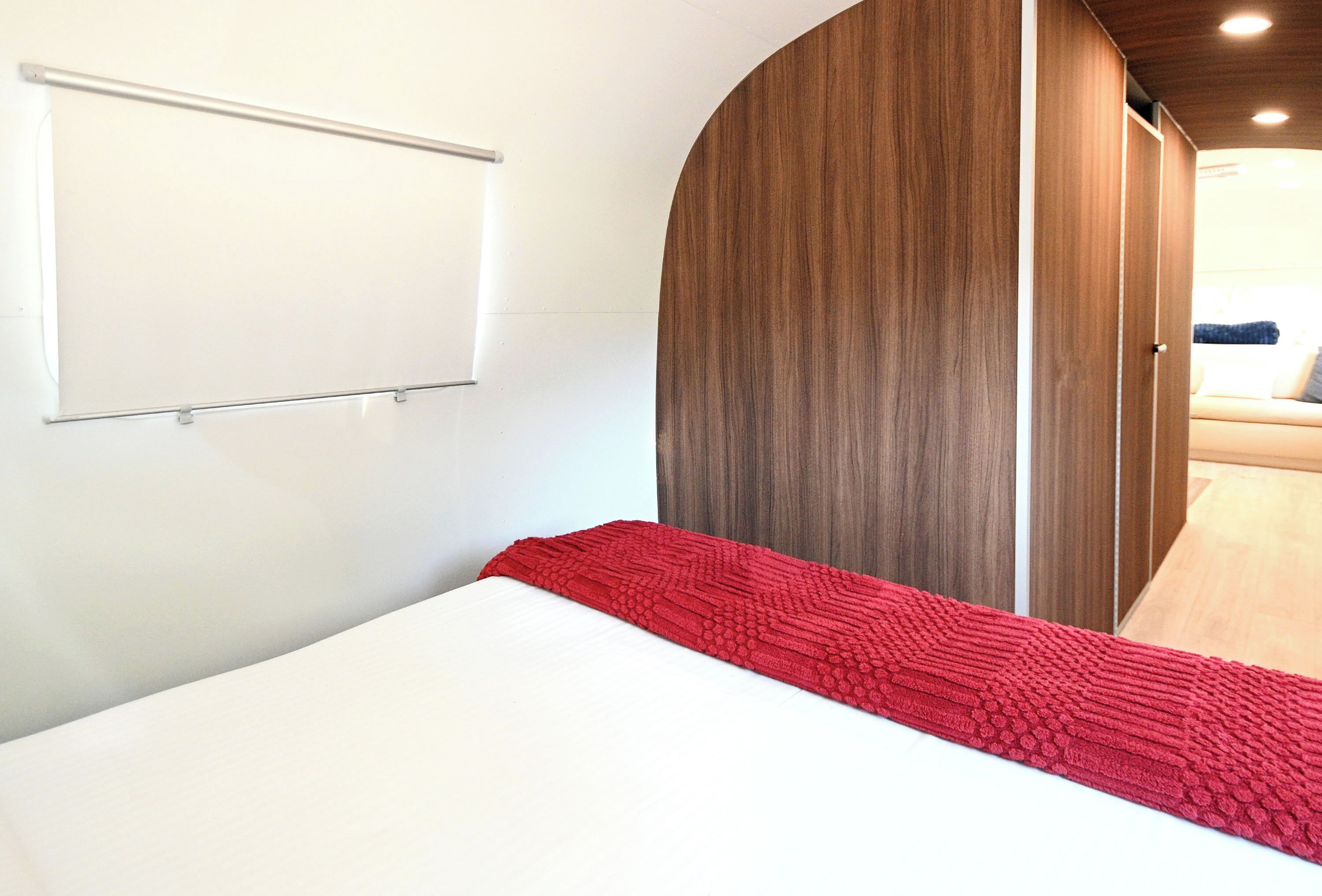 A bed with a red blanket, a white wall, and a wooden wardrobe.