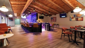 A bar area with wooden ceiling beams, multiple hanging pendant lights, and a bar counter with stools. - Village Inn  (Lompoc)
