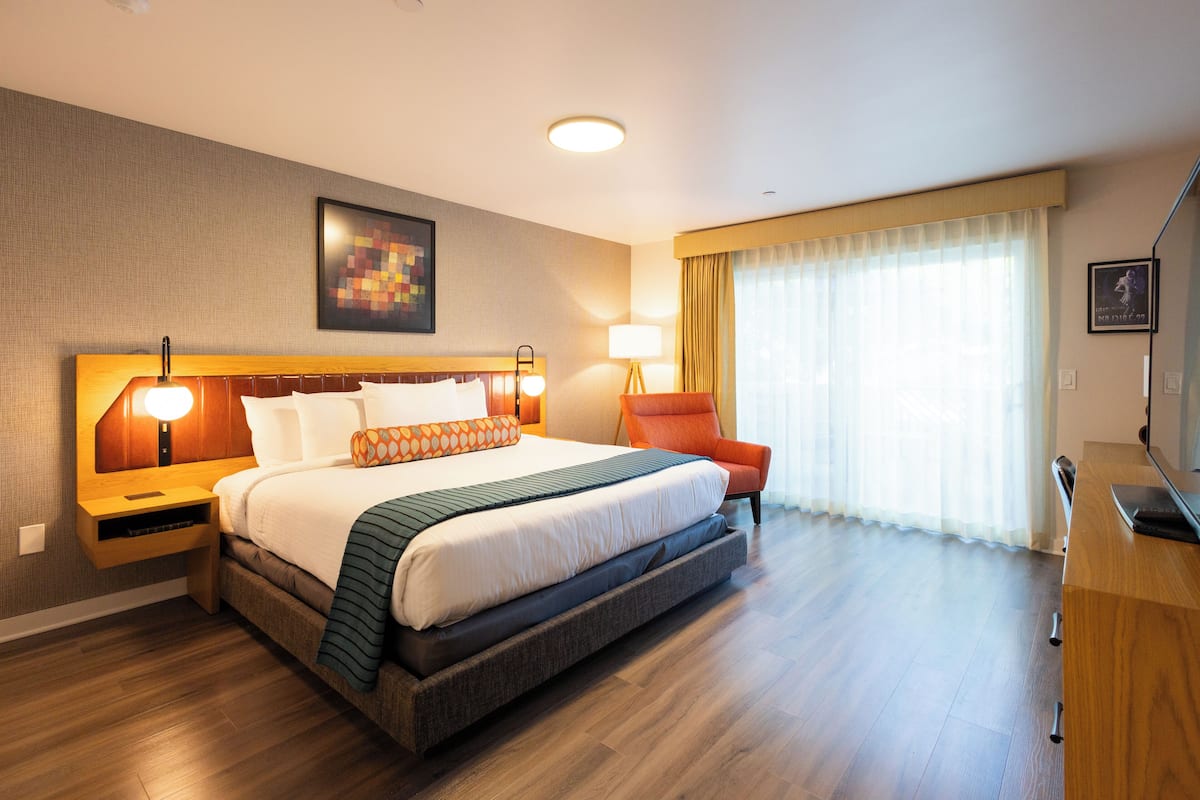 A modern hotel room with a large bed, a wooden nightstand, a desk, and a chair.