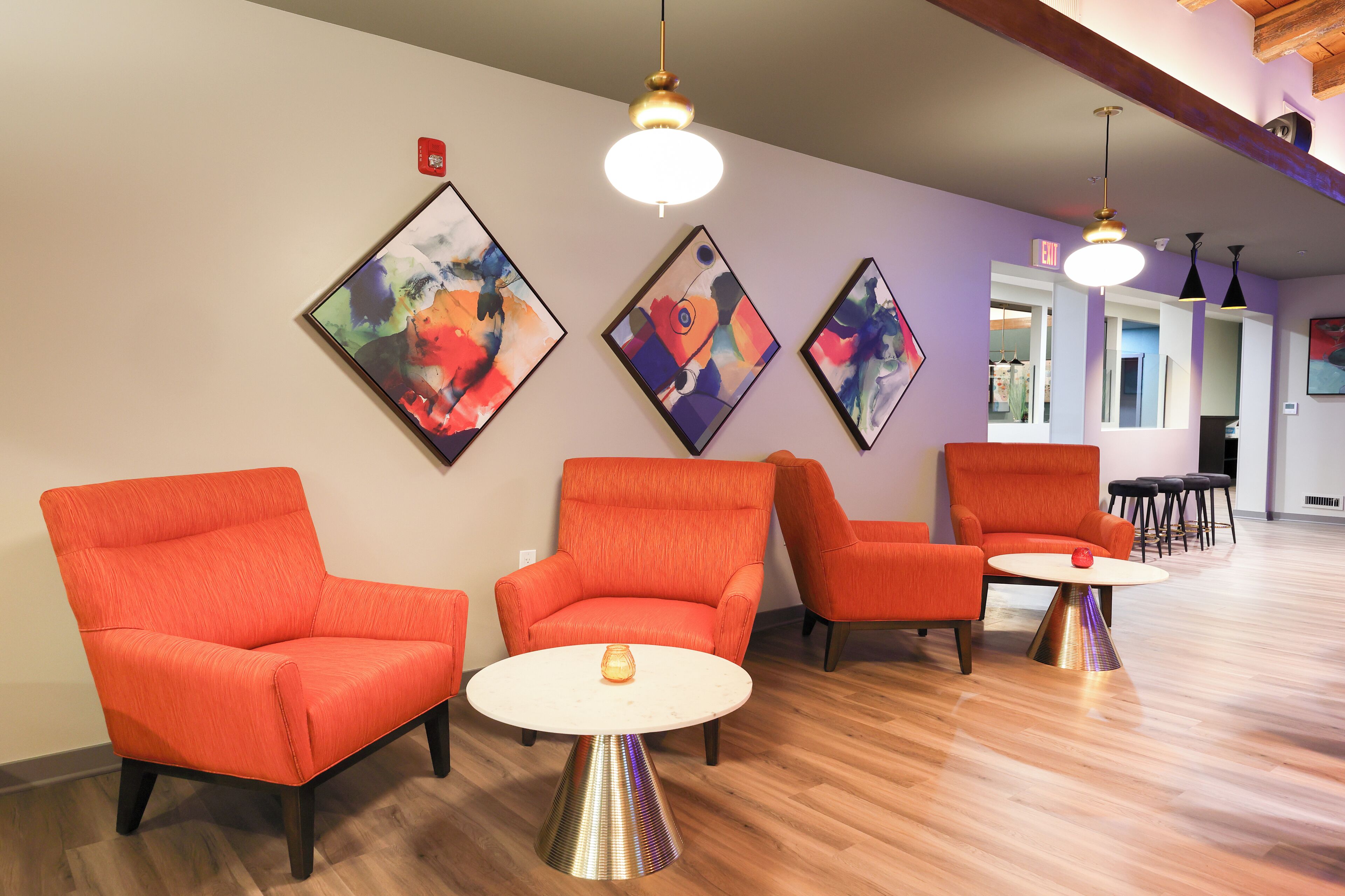 Un espace de détente moderne avec des fauteuils orange et une table blanche, agrémenté d’œuvres d’art abstraites aux murs et d’un éclairage suspendu.