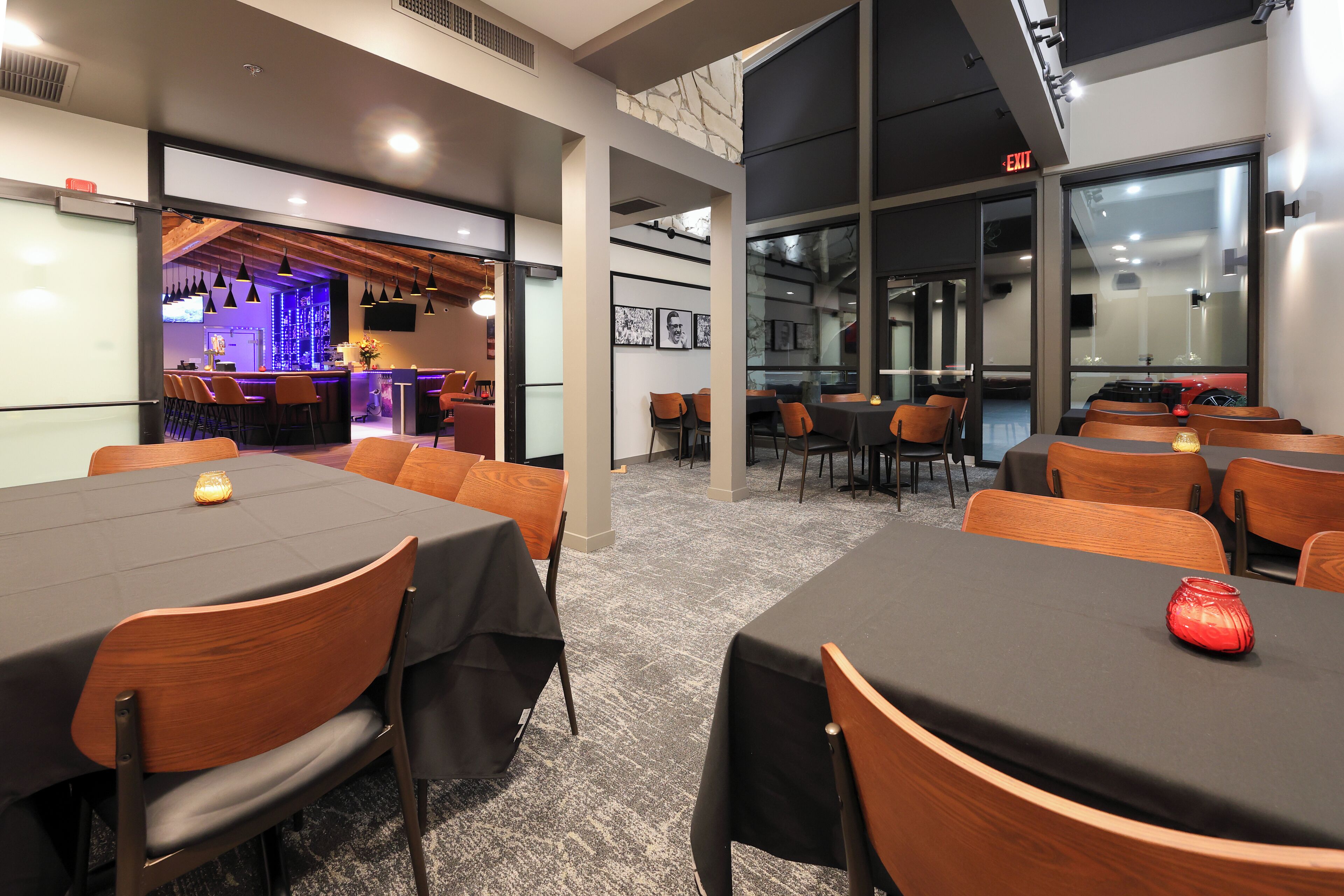 A conference room with tables and chairs, a bar area in the background, and a large window.