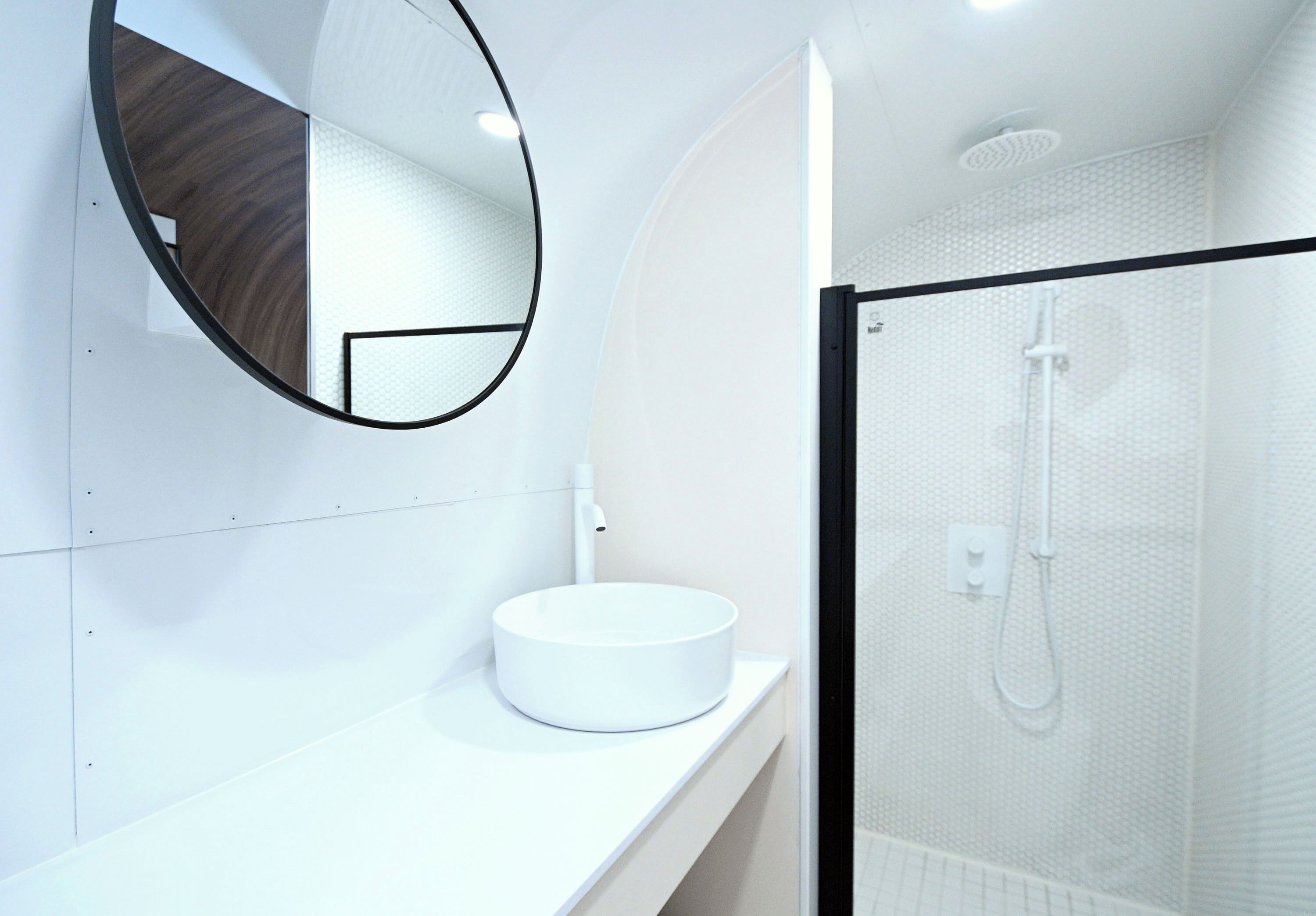 Une salle de bain moderne avec un lavabo rond blanc, un miroir et une douche à parois de verre.