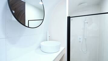 A modern bathroom with a round white sink, a mirror, and a glass-enclosed shower.
