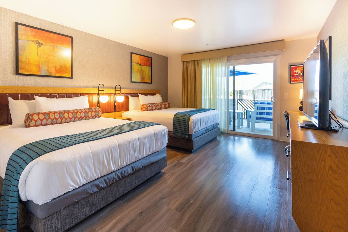 A hotel room with two beds, a TV, and a balcony with a view.