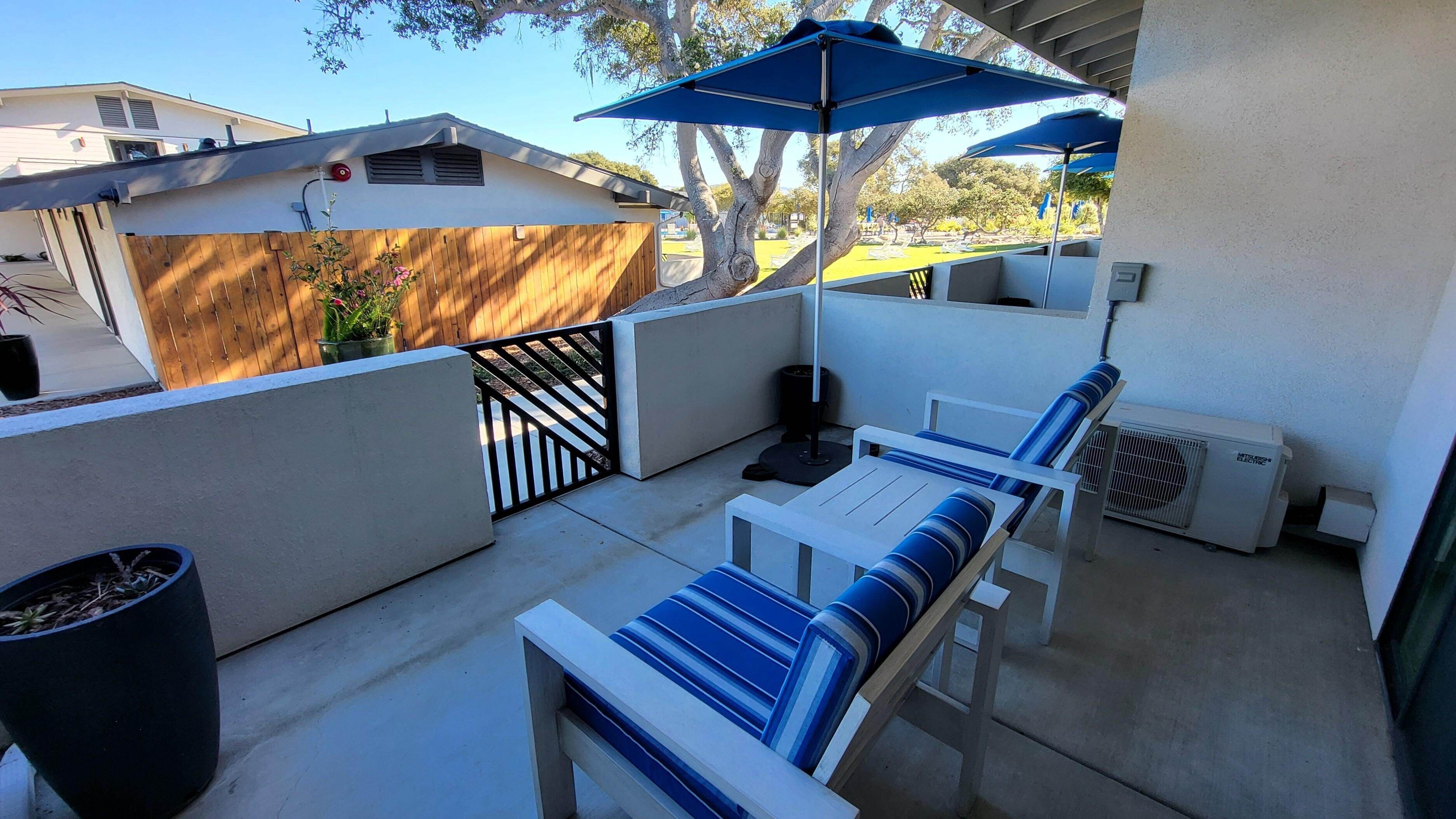 Um pátio com mesa e cadeiras, um cesto de lixo e um guarda-sol azul.